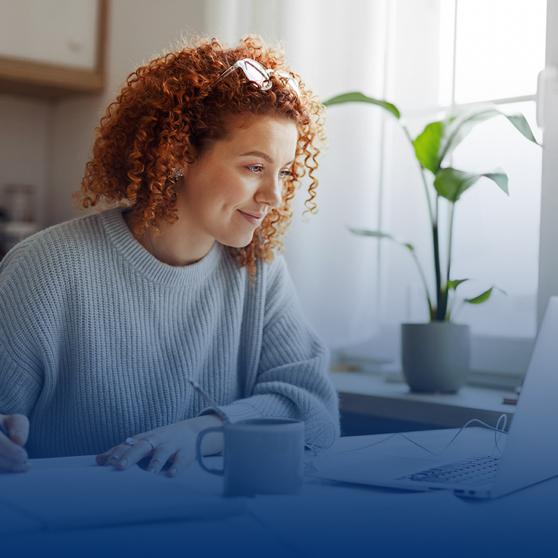 woman-with-curly-red-hair-takes-notes-while-looking-at-computer-screen